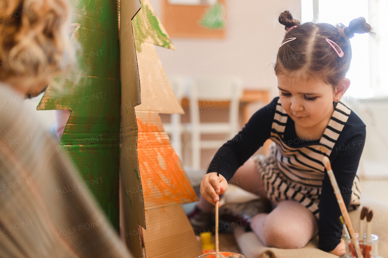 Little girl painting a cardboard tree at creative art and craft class at school