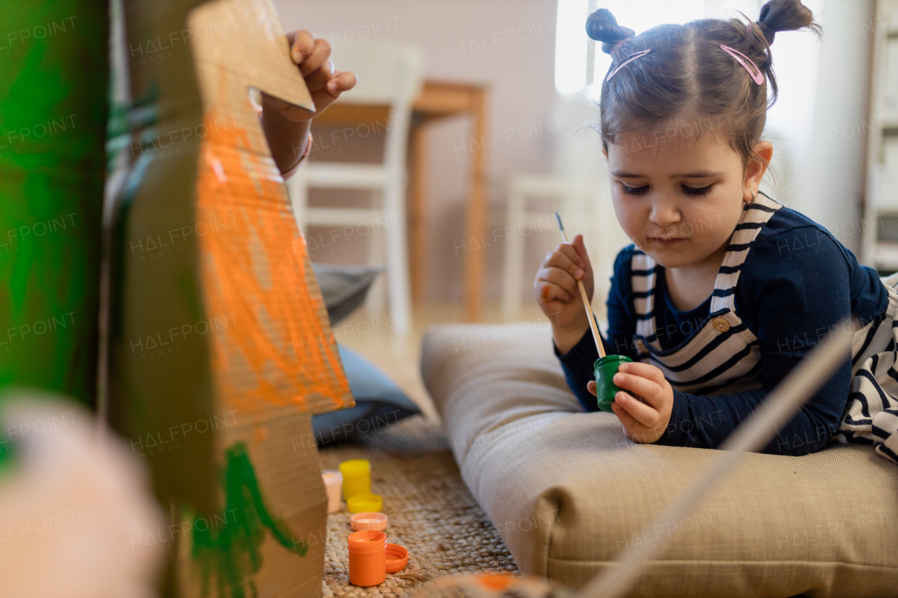 Little girl painting a cardboard tree at creative art and craft class at school