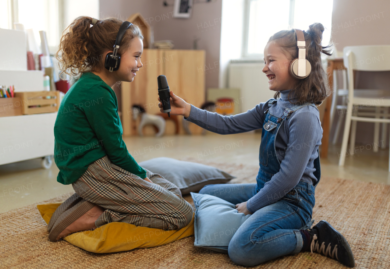 Happy little girls with headphones and microphone taking an interview, having fun and playing at home.