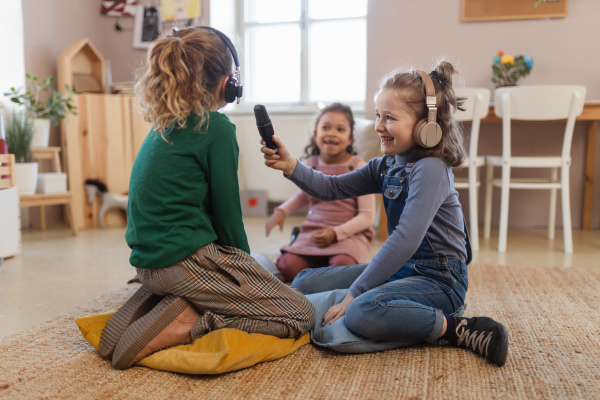 Happy little girls with headphones and microphone taking an interview, having fun and playing at home.