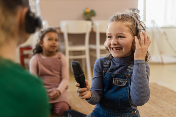 Happy little girls with headphones and microphone taking an interview, having fun and playing at home.