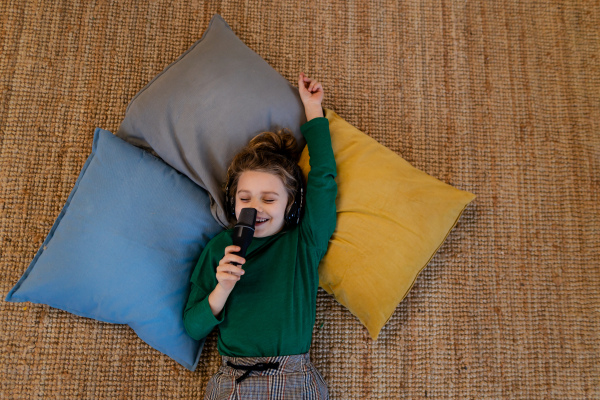 A little girl lying on the floor on cushions listening music,singing having fun and playing at home.