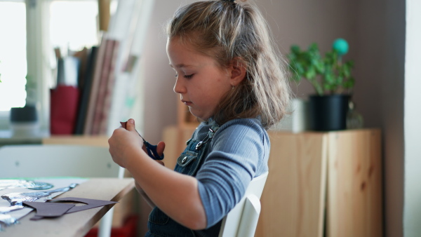 A happy little girl cutting paper with scissors during creative art and craft class at school.