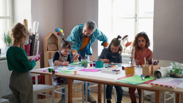 A group of little kids working on project with teacher during creative art and craft class indoors at school.