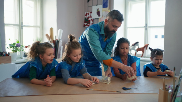 A group of little kids with teacher working with pottery clay during creative art and craft class at school.