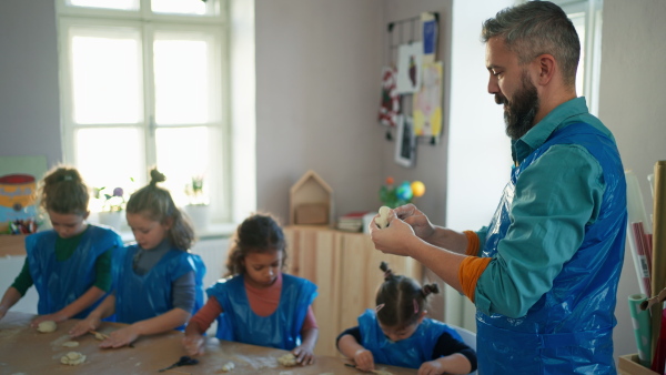 A group of little kids with teacher working with pottery clay during creative art and craft class at school.