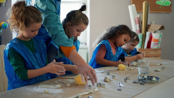 A group of little kids with teacher working with pottery clay during creative art and craft class at school.