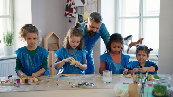 A group of little kids with teacher working with pottery clay during creative art and craft class at school.