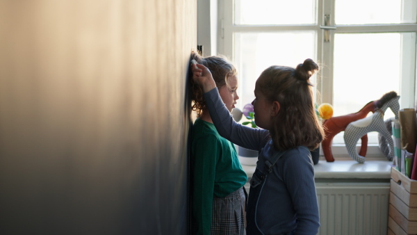 A little girl drawing her friends with chalks on blackboard wall indoors in playroom.