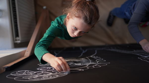 Little girls drawing with chalks on a blackboard wall indoors in playroom.