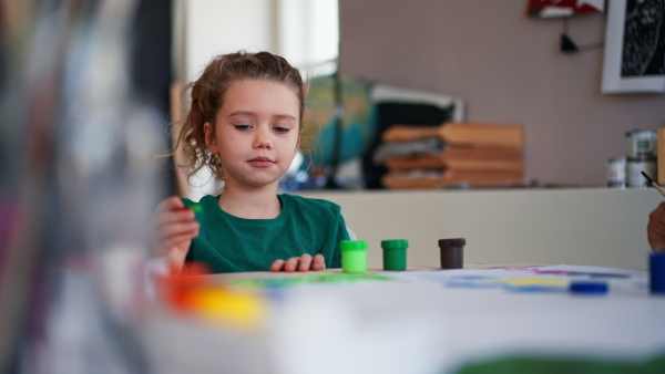 A happy little girl painting picture during creative art and craft class at school.