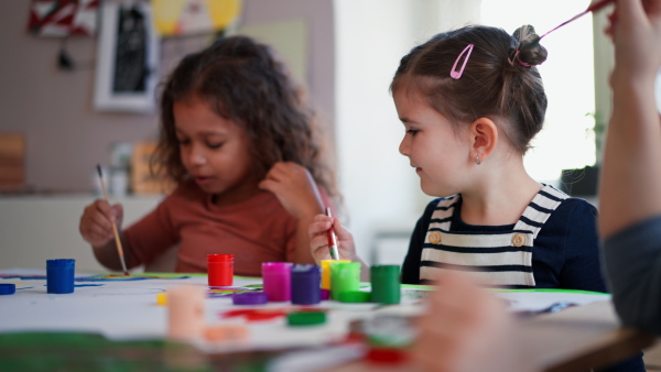 Happy little girls painting a picture during creative art and craft class at school.