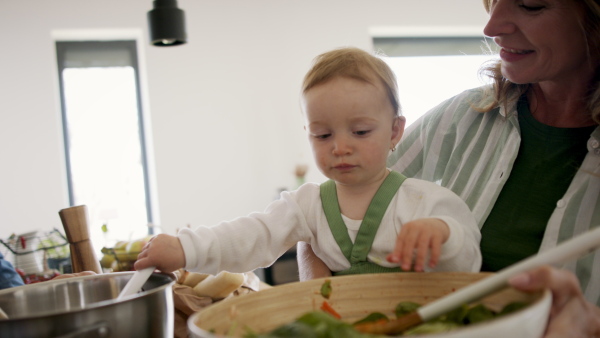 Grandparents cooking with small granddaughter indoors at home.