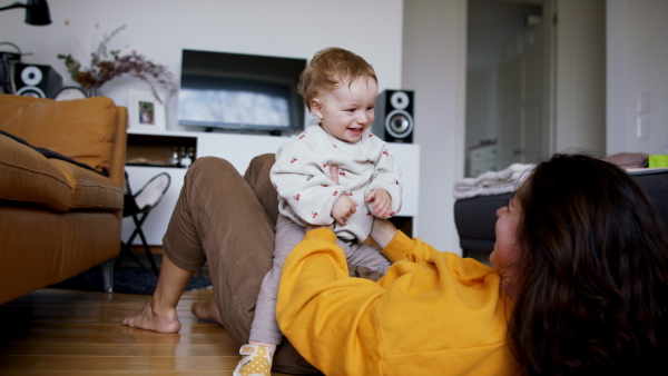 A young mother playing with small baby indoors at home, having fun.