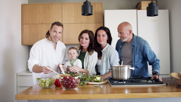 Happy multigeneration family indoors at home preparing vegetable salad in kitchen, looking at camera.