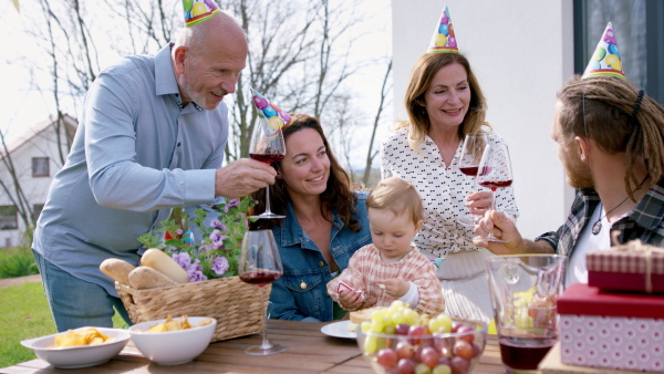 A happy multigeneration family outdoors in garden at home, birthday celebration party.