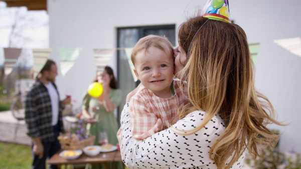 A grandmother with granddaughter outdoors in garden at home, birthday celebration party.