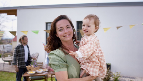 A mother with daughter outdoors in garden at home, looking at camera. Birthday celebration party.