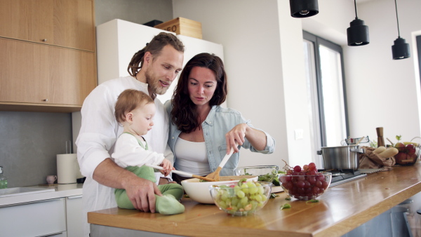 Happy family indoors at home preparing vegetable salad in kitchen.