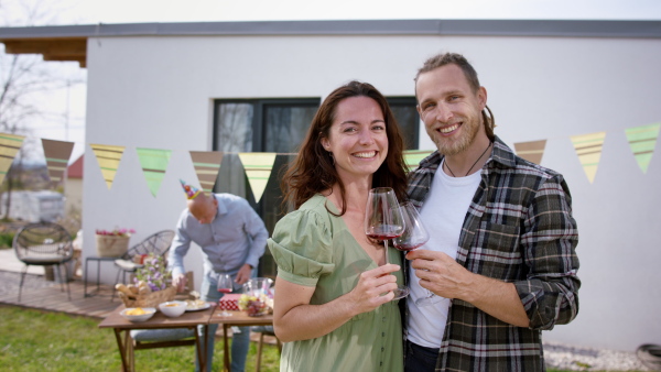 A young couple with wine outdoors in garden at home, birthday celebration party.