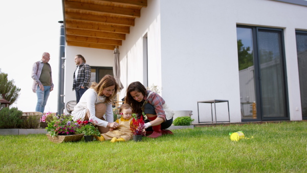 A happy multigeneration family outdoors planting flowers in garden at home, gardening concept.