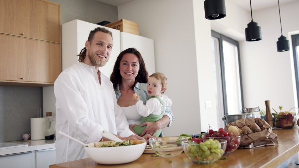 Happy family indoors at home preparing vegetable salad in kitchen, looking at camera.