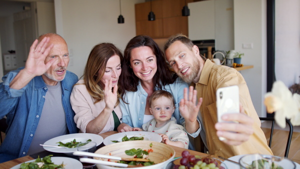 Happy multigeneration family indoors at home eating healthy lunch, taking a video with smartphone.