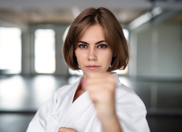 An attractive young woman practising karate indoors in gym.