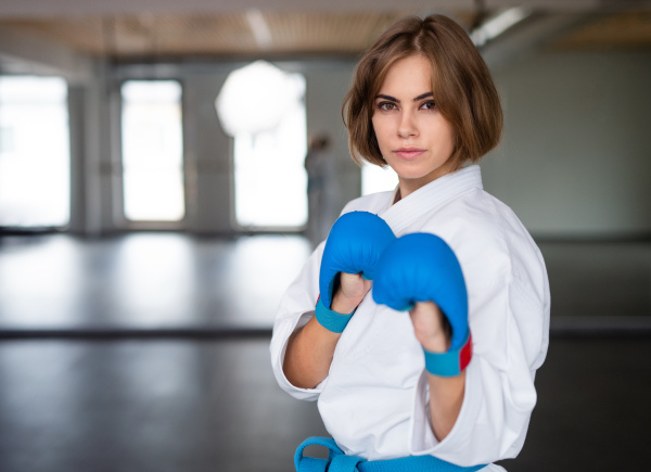 An attractive young woman practising karate indoors in gym.