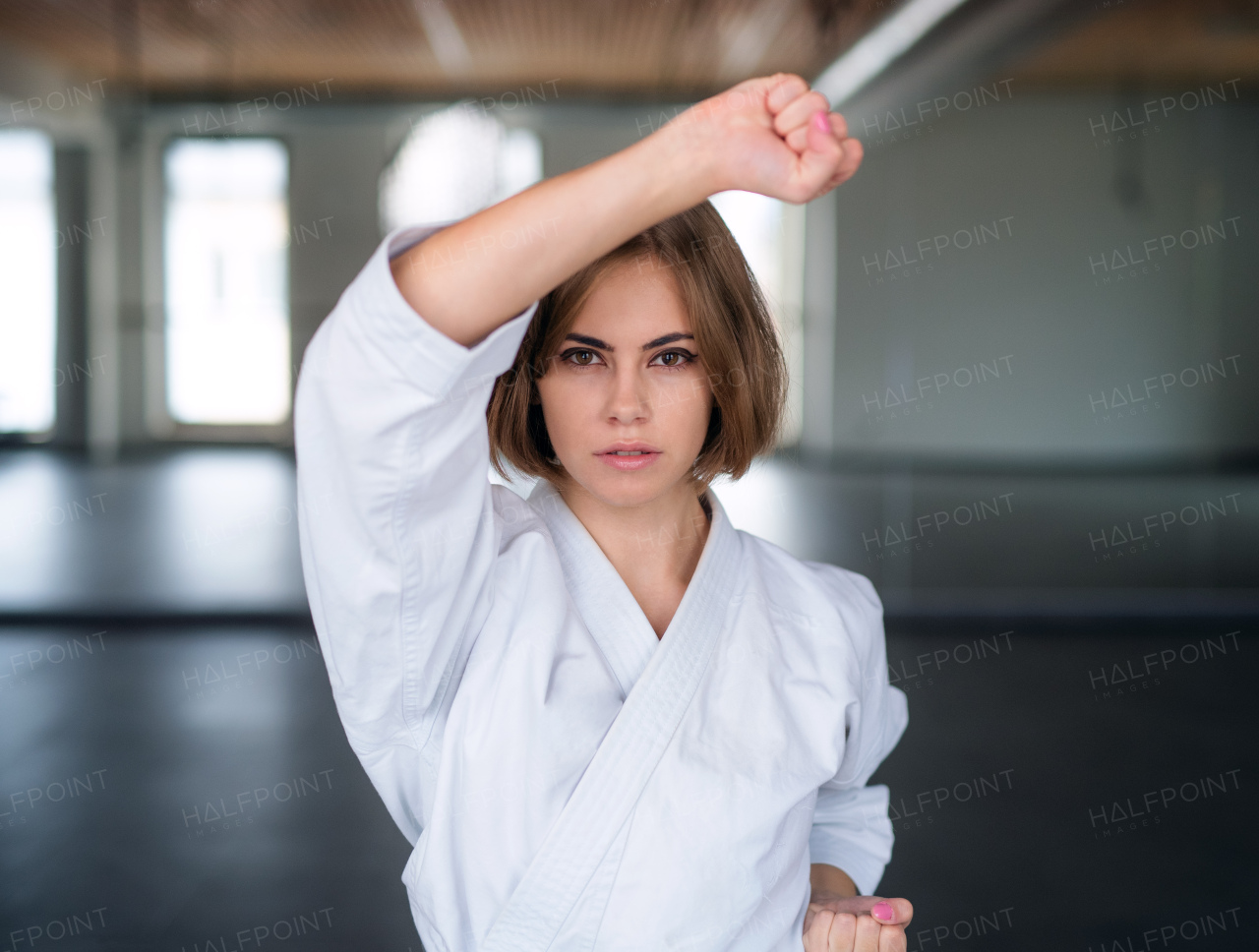 An attractive young woman practising karate indoors in gym.