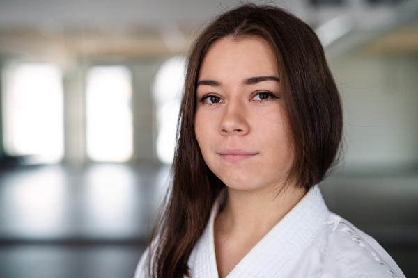 A portrait of young karate woman standing indoors in gym, looking at camera.