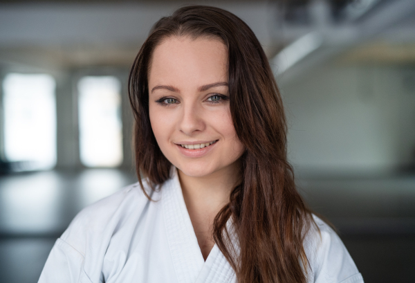 A portrait of young karate woman standing indoors in gym, looking at camera.