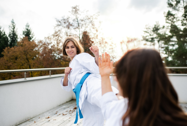 Two young women practising karate outdoors on terrace.