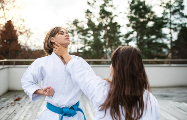 Two young women practising karate outdoors on terrace.