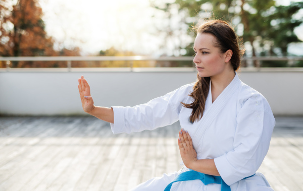 An attractive young woman practising karate outdoors on terrace.