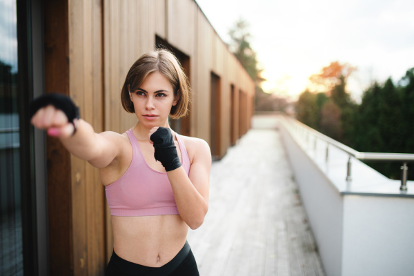 A front view of young woman practising karate outdoors on terrace.