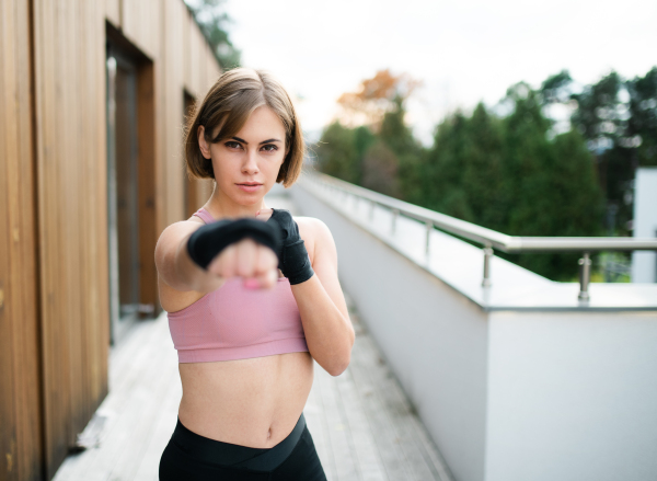 A front view of young woman practising karate outdoors on terrace.