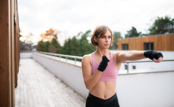 A front view of young woman practising karate outdoors on terrace.