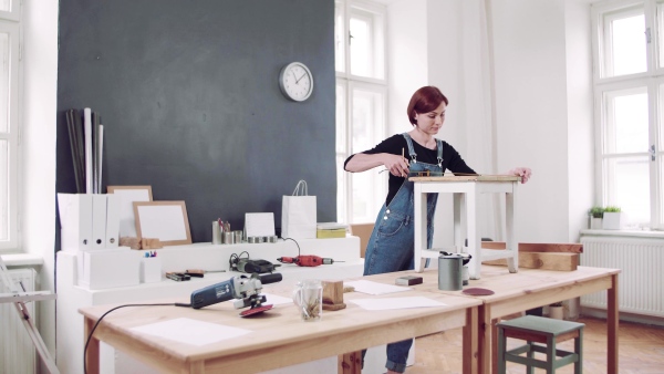 Young woman standing indoors restoring old furniture.