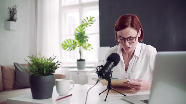 A front view of young woman indoors, recording a podcast at home. Slow motion.