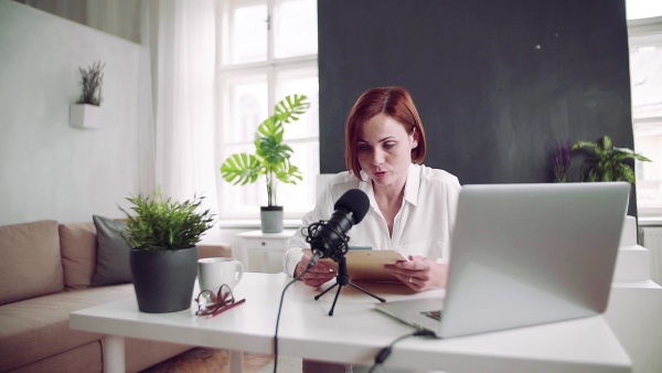 A front view of young woman indoors, recording a podcast at home. Slow motion.