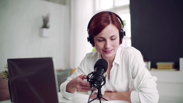 A front view of young woman indoors, recording a podcast at home. Slow motion.