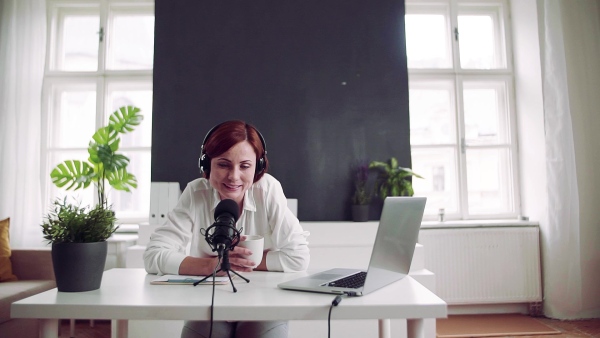 A front view of young woman indoors, recording a podcast at home. Slow motion.