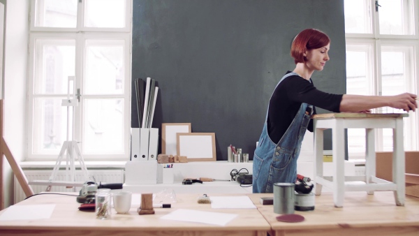 Young woman standing indoors restoring old furniture.