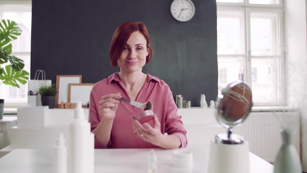 Front view of young woman vlogger showing how to apply makeup indoors, video about beauty products.