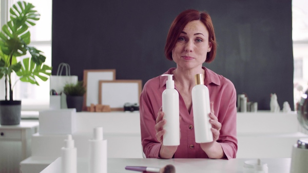 A front view of young woman vlogger indoors, making video about beauty products.