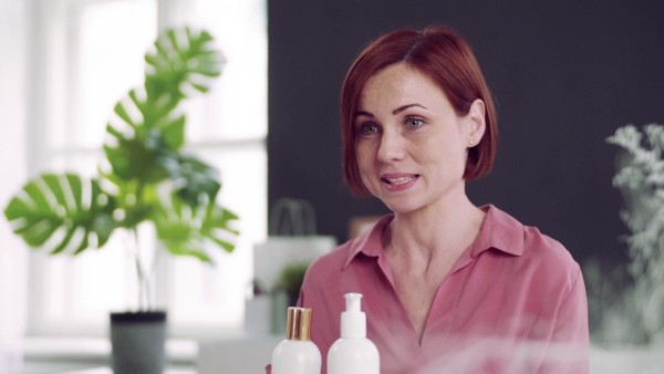 A front view of young woman vlogger indoors, making video about beauty products.