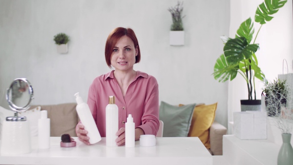 A front view of young woman vlogger indoors, making video about beauty products.