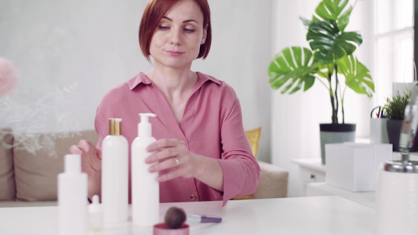 A front view of young woman vlogger indoors, making video about beauty products.