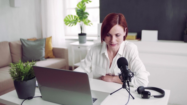 A front view of young woman indoors, recording a podcast at home.